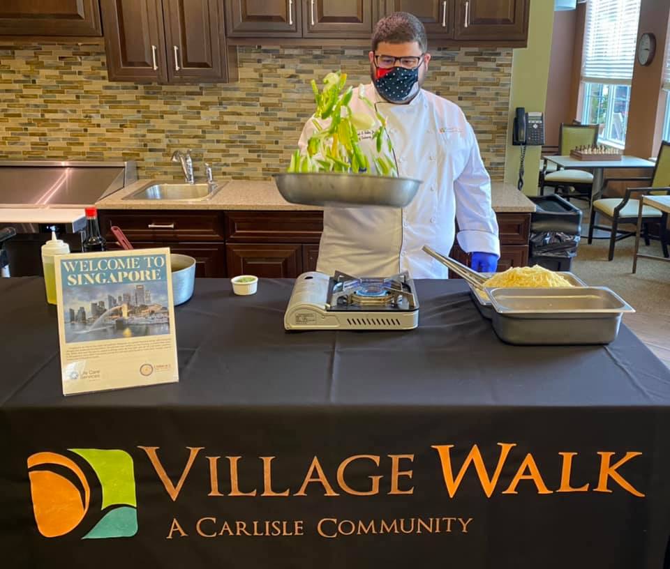 A chef providing a level of care in an assisted living community and flicking vegetables in a wok in the air.