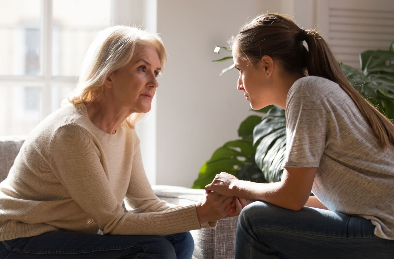 An older adult woman and her daughter having a serious conversation with each other in a sunlit room