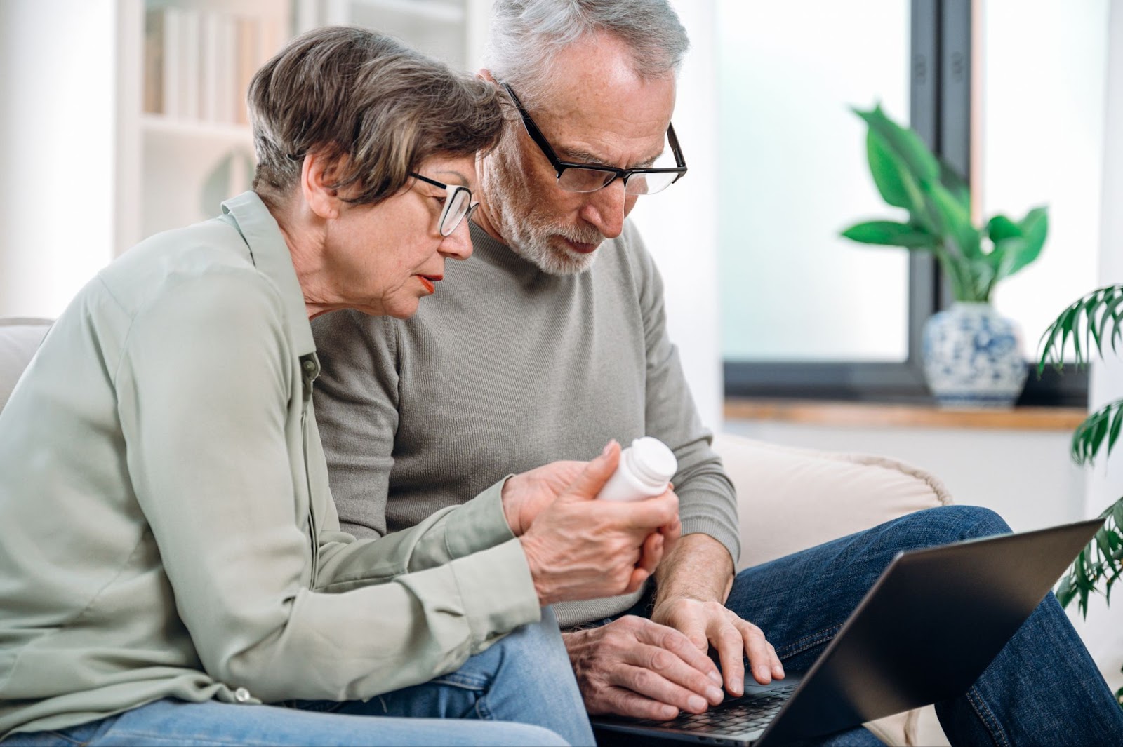 Senior couple, male and female, looking at prescription and laptop on couch. - Understanding Medicare's Role in Your Financial Future blog image