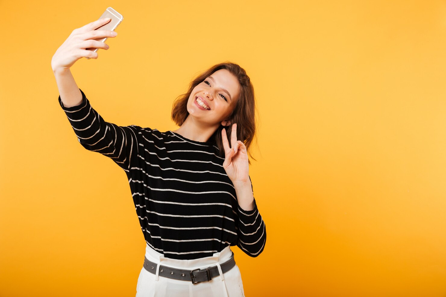 A woman making a victory sign while posing for a selfie.