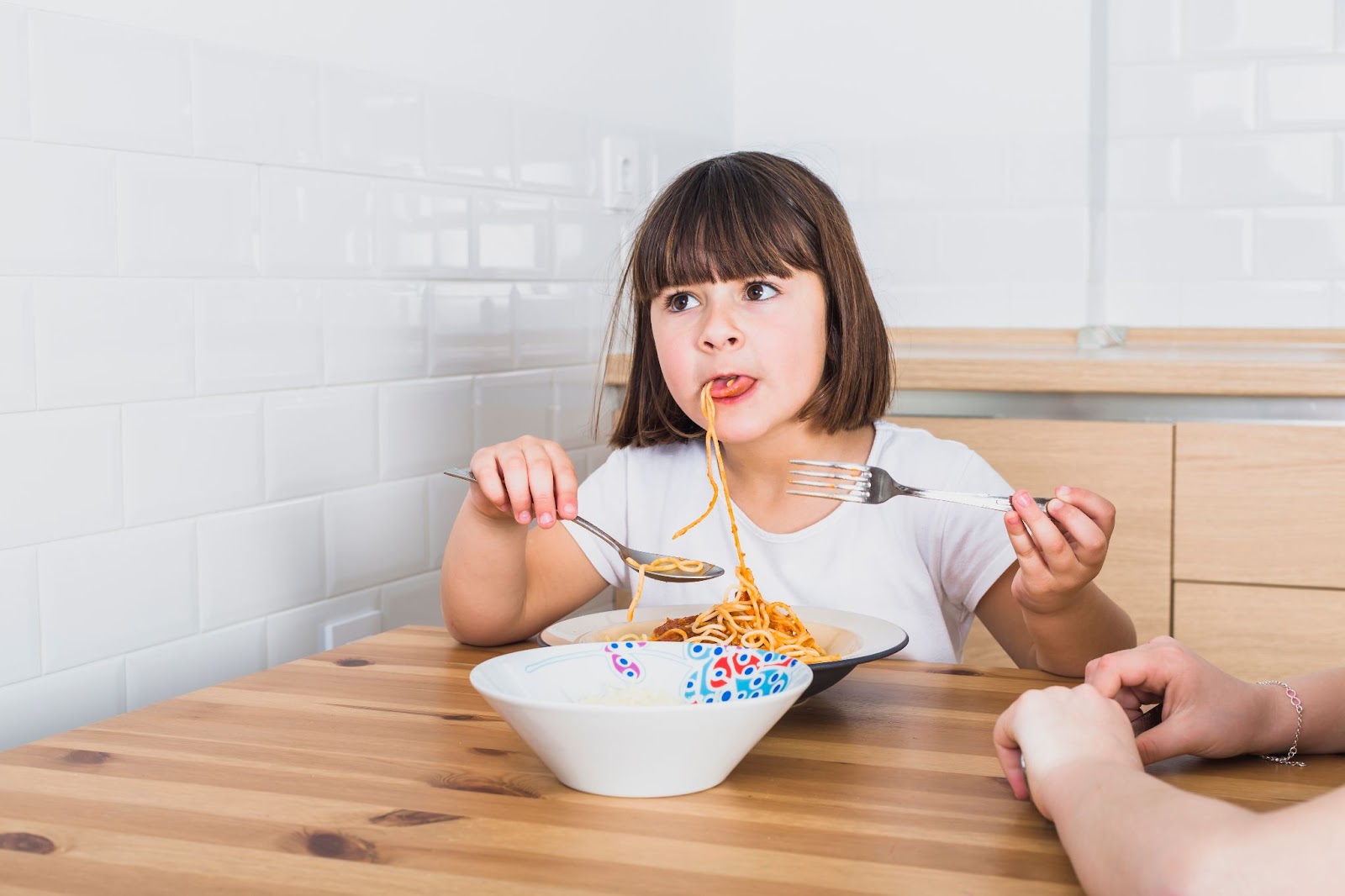 Seorang gadis kecil sedang makan spaghetti dengan garpu.