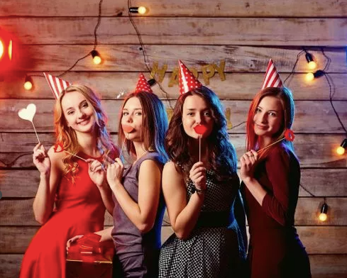 Four girls wearing party hats and holding party props, posing joyfully at a birthday party event.