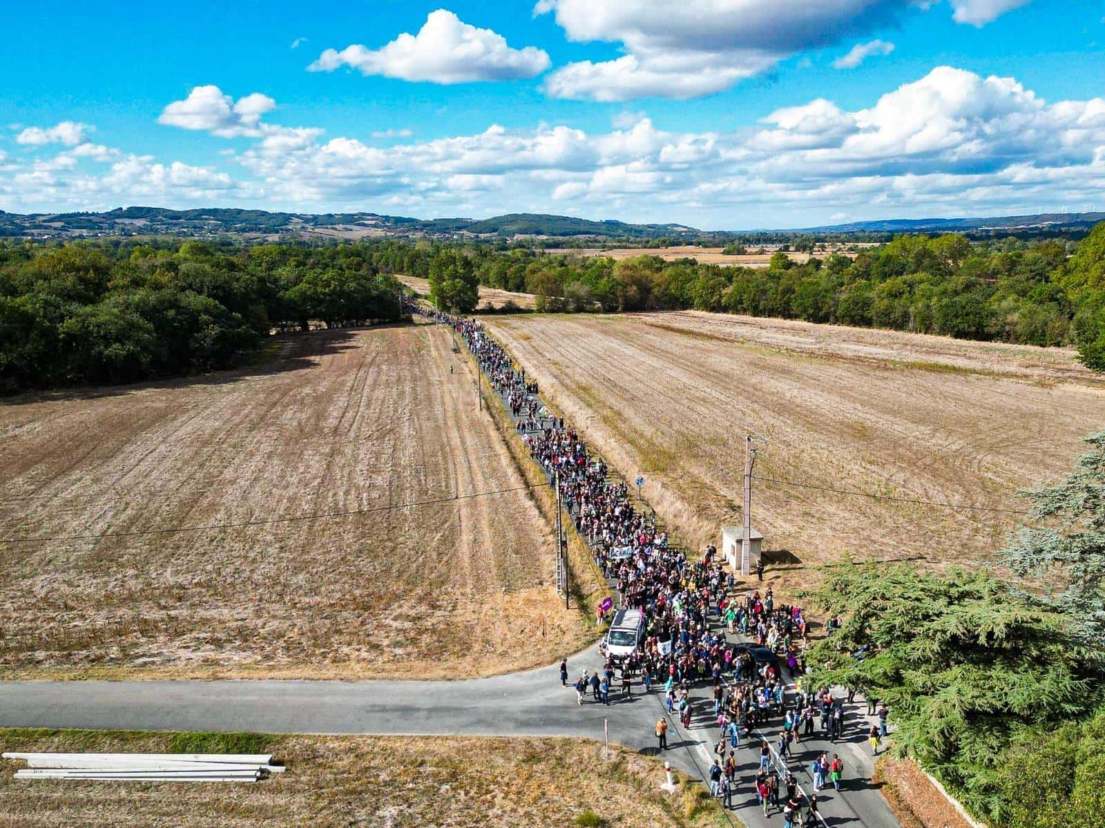 A long column of activists march down a country road, dry fields either side
