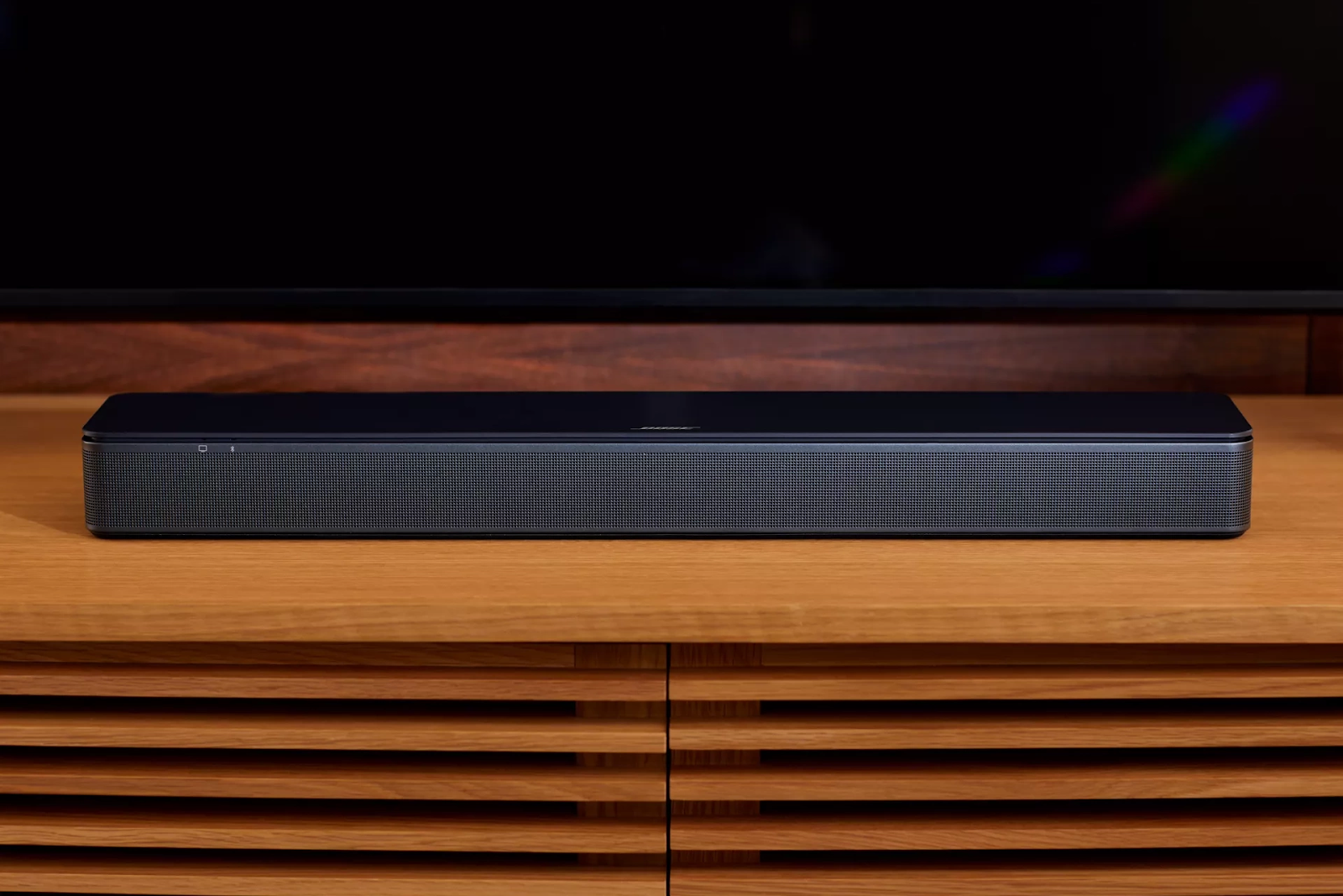 A front view of the Bose TV Speaker placed on a wooden table. 