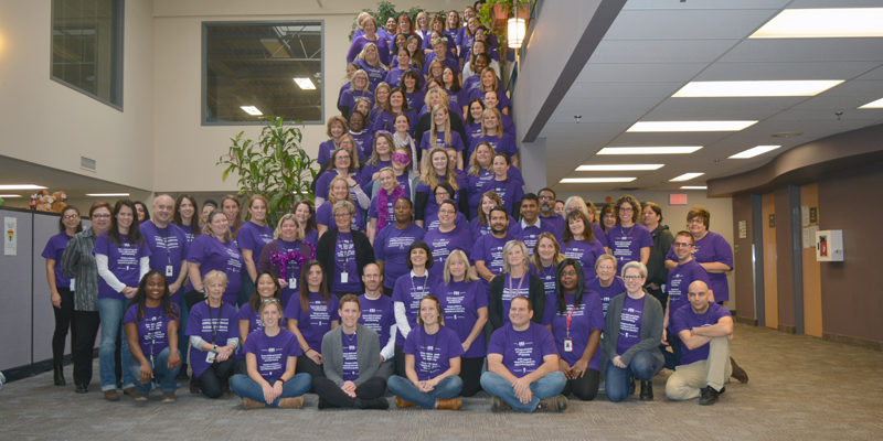 A group of LSU School of Medicine students wearing purple t-shirts and volunteering at a community service event, distributing food and interacting with community members.