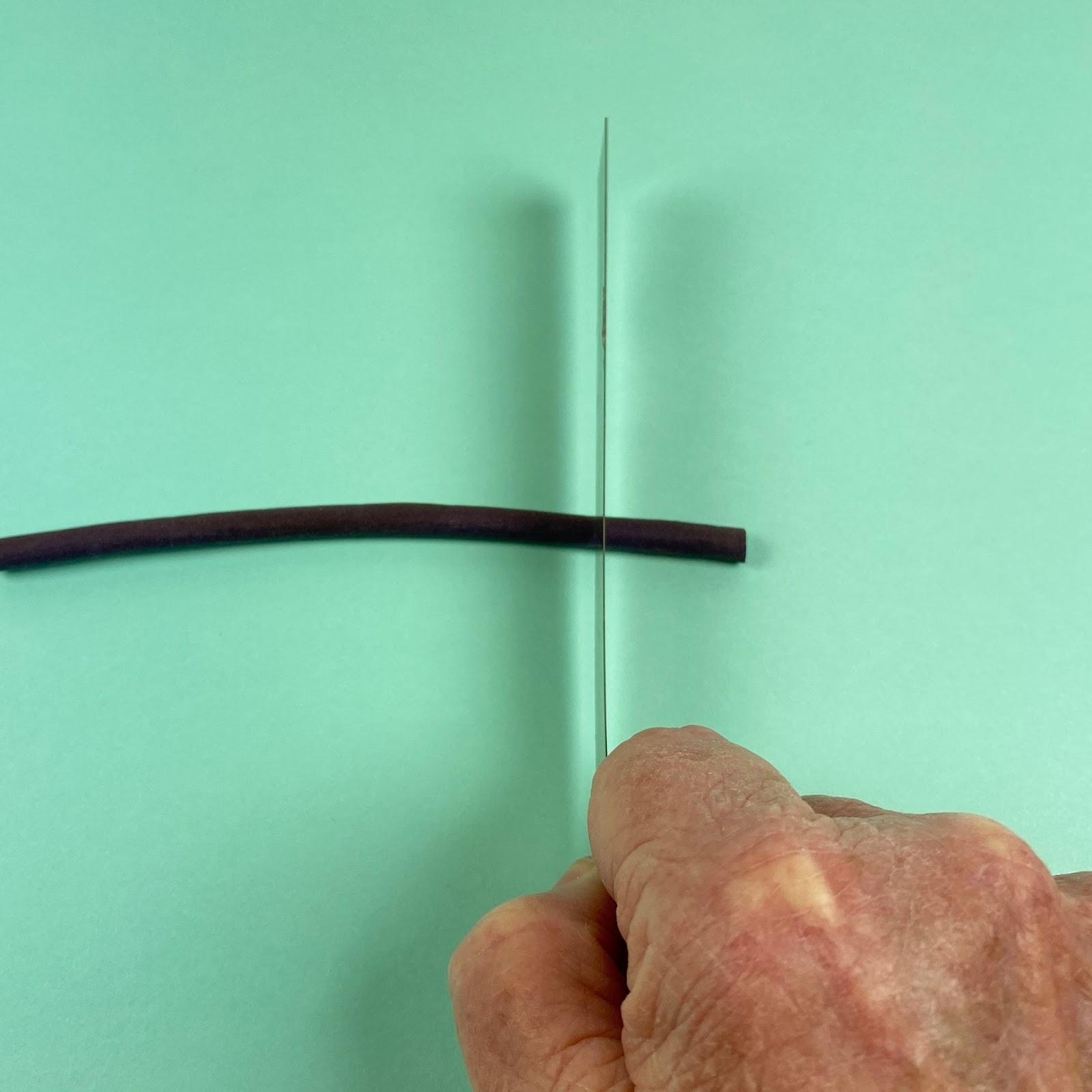 Photo showing a tissue blade being used to cut a piece off of a cured hollow tube of polymer clay