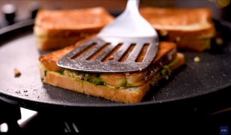 Sandwiches being toasted on a tawa with butter applied on both sides for a crispy texture.