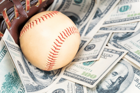 A baseball resting in a glove with hundred-dollar bills