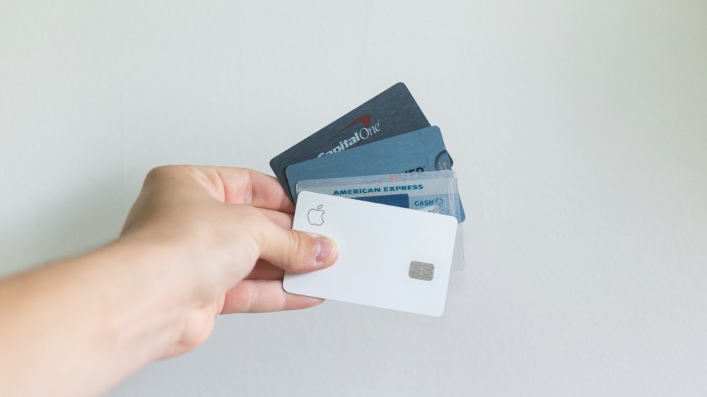 A hand holding up a variety of credit and debit cards - Debit & Credit Cards: Pros & Cons
