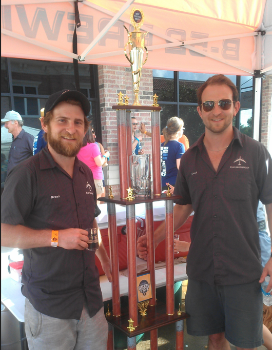 Two men standing next to a trophy

Description automatically generated