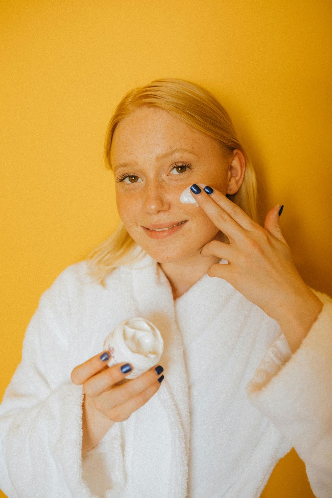 white woman with strawberry blonde har applying ayurveda based facial moisturizer.
