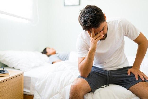 Free photo thoughtful young man in pjs sitting up in bed in the morning and feeling sad with his bad relationship