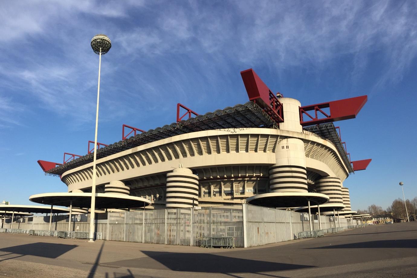 A large stadium with a fence and a light post with San Siro in the background

Description automatically generated