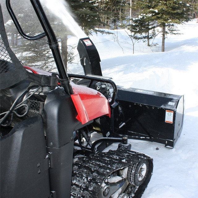 An image taken from just to the side of the cab of a UTV on a snowy trail, facing the front end of the vehicle with the Can-Am Defender Vantage Snowblower by Bercomac mounted.