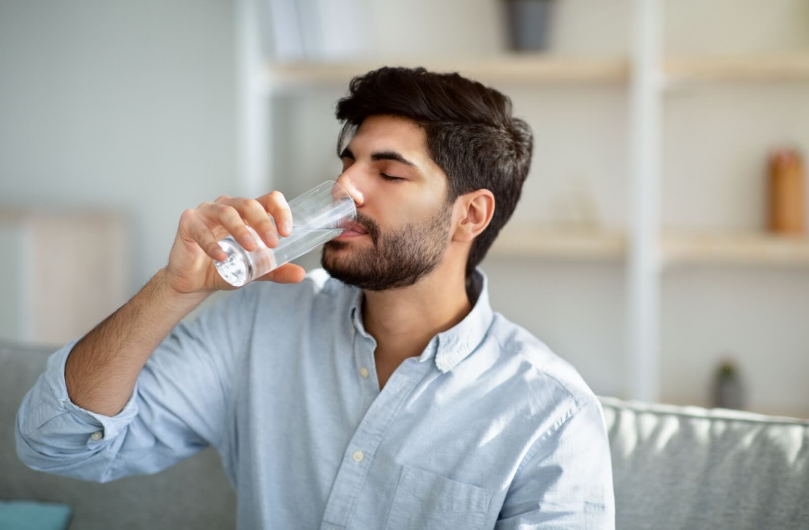 A man drinking water from a glass in sunlit room.
