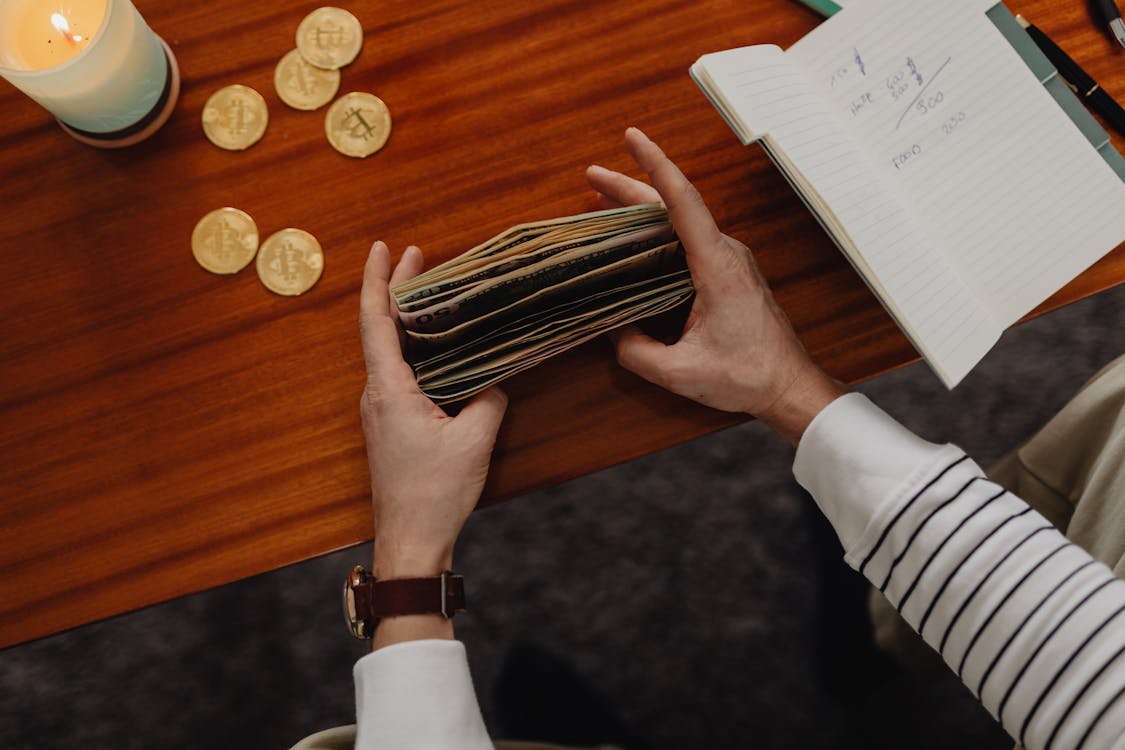 Free Person Counting Bills and Bitcoins on Table Stock Photo