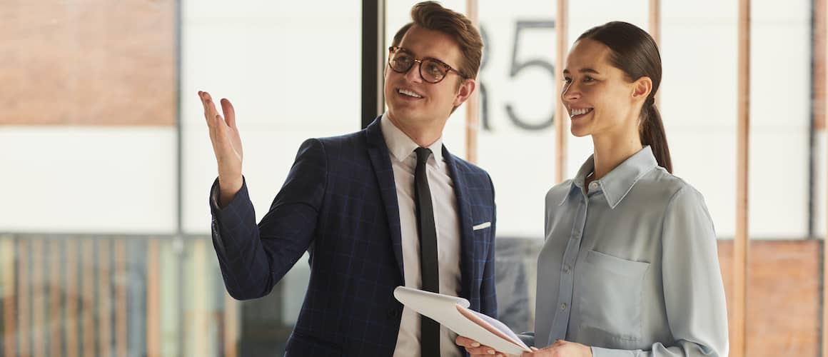 A guy in a navy blue suit paired with a white shirt is trying to show a woman her dream house.