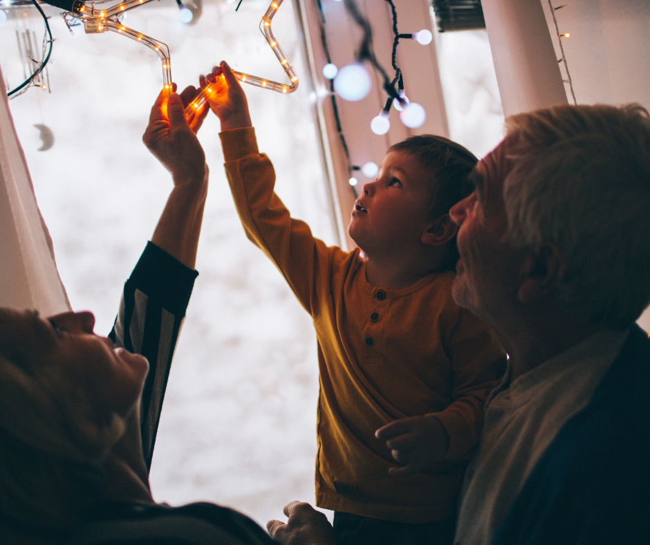 Two people letting a toddler hang a Christmas star