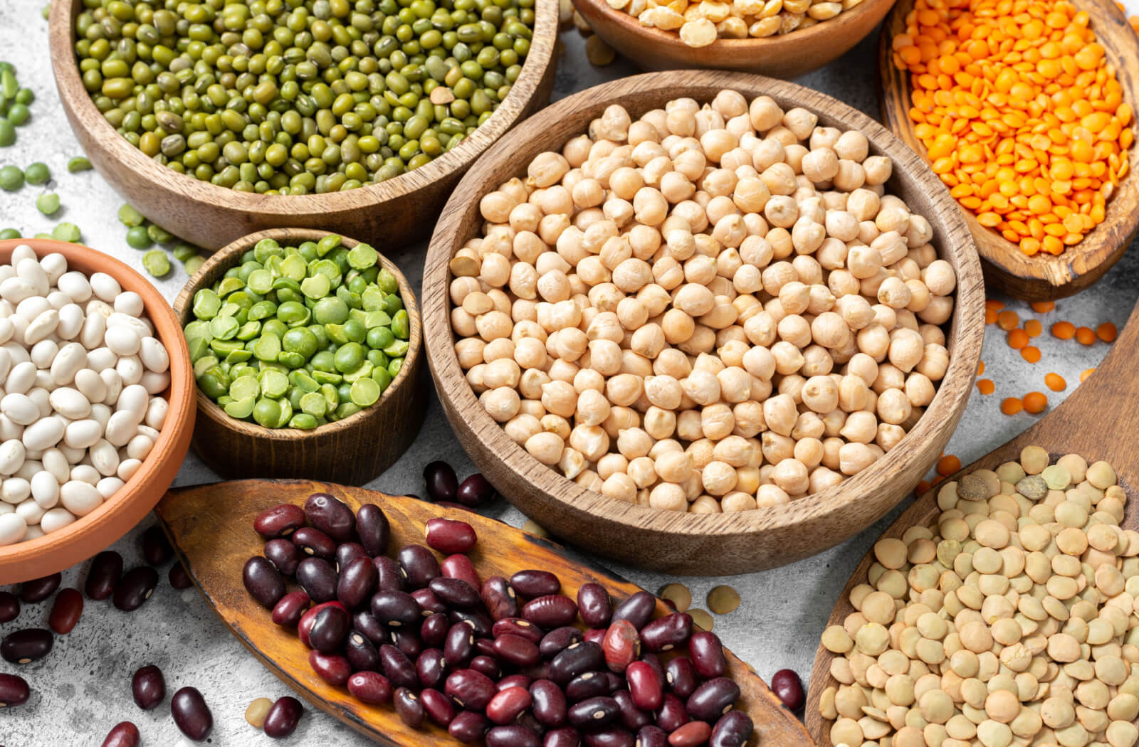 An assortment of various beans sorted into different wooden bowls.