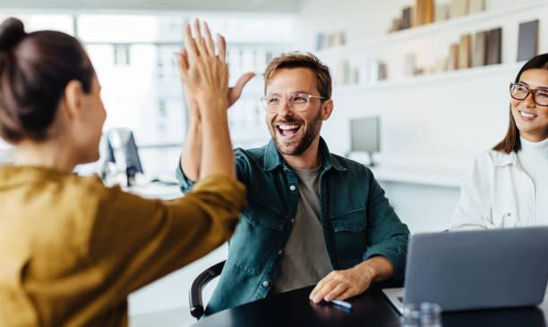 Business people celebrating success in an office Successful business people giving each other a high five in a meeting. Two young business professionals celebrating teamwork in an office. busines man stock pictures, royalty-free photos & images