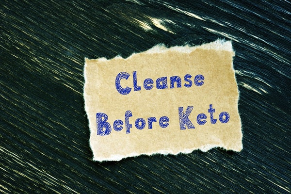 A piece of brown paper with the words "Cleanse Before Keto" written on it with a blue pen