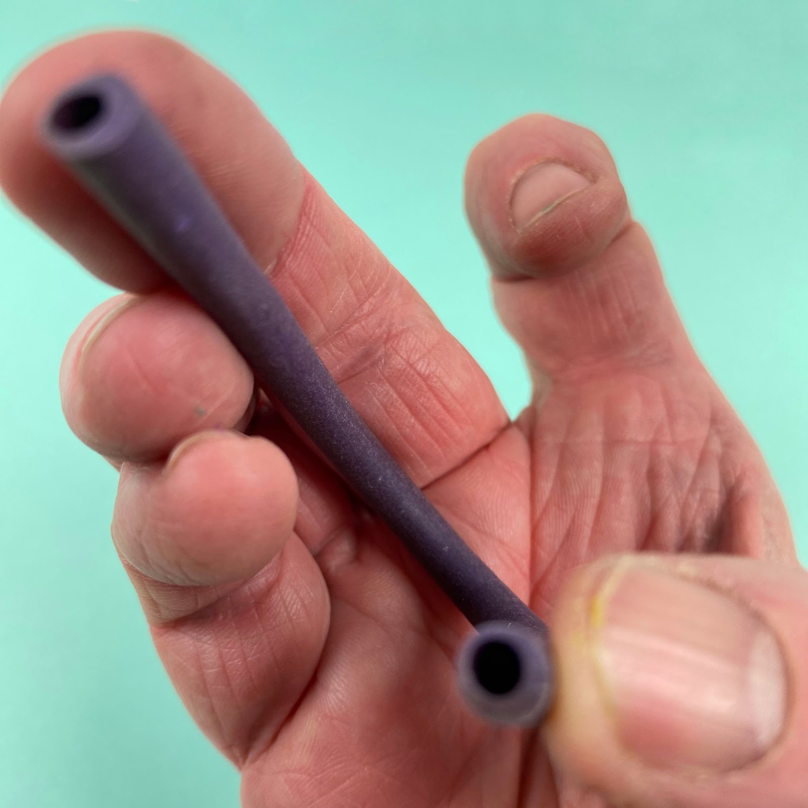 Photo of a baked hollow polymer clay tube bent into a U shape, showing its flexibility