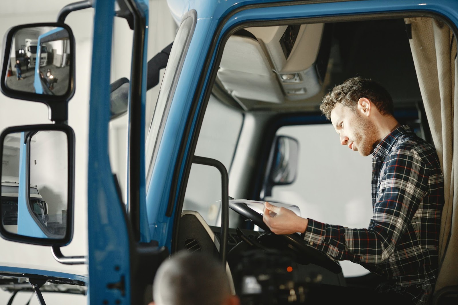 A man sitting in the front seat of a semi-truck looking at a paper on the steering wheel