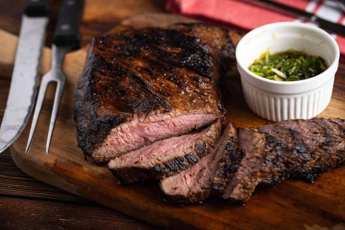 Tăiați felii tri-tip, pe o masă de tăiat cu un cuțit și ramekin de chimichurri