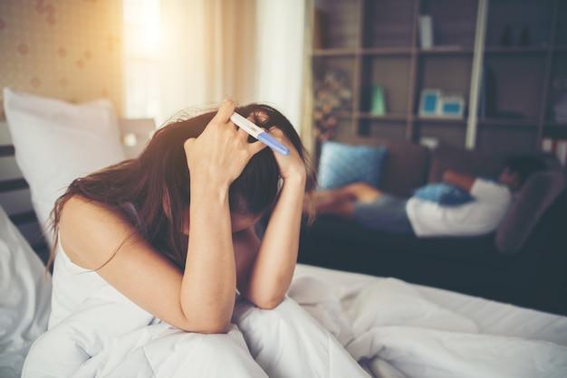 Free photo sad woman complaining holding a pregnancy test sitting on bed