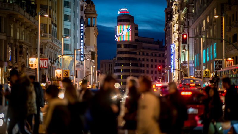 Bustling nighttime street scene with neon lights and a crowd of pedestrians in Madrid.
