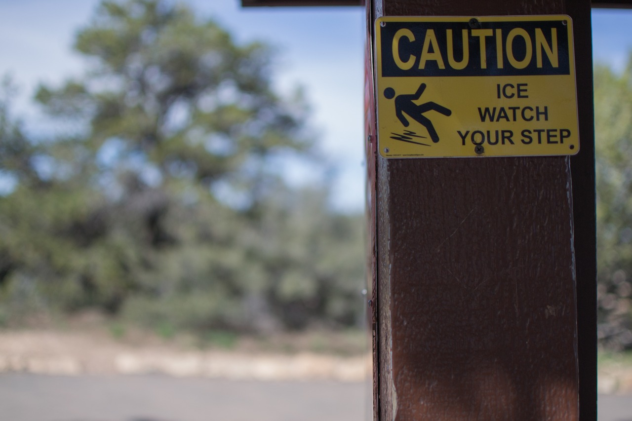 a cautionary sign affixed to a post along the roadside, warning pedestrians to be cautious due to icy conditions