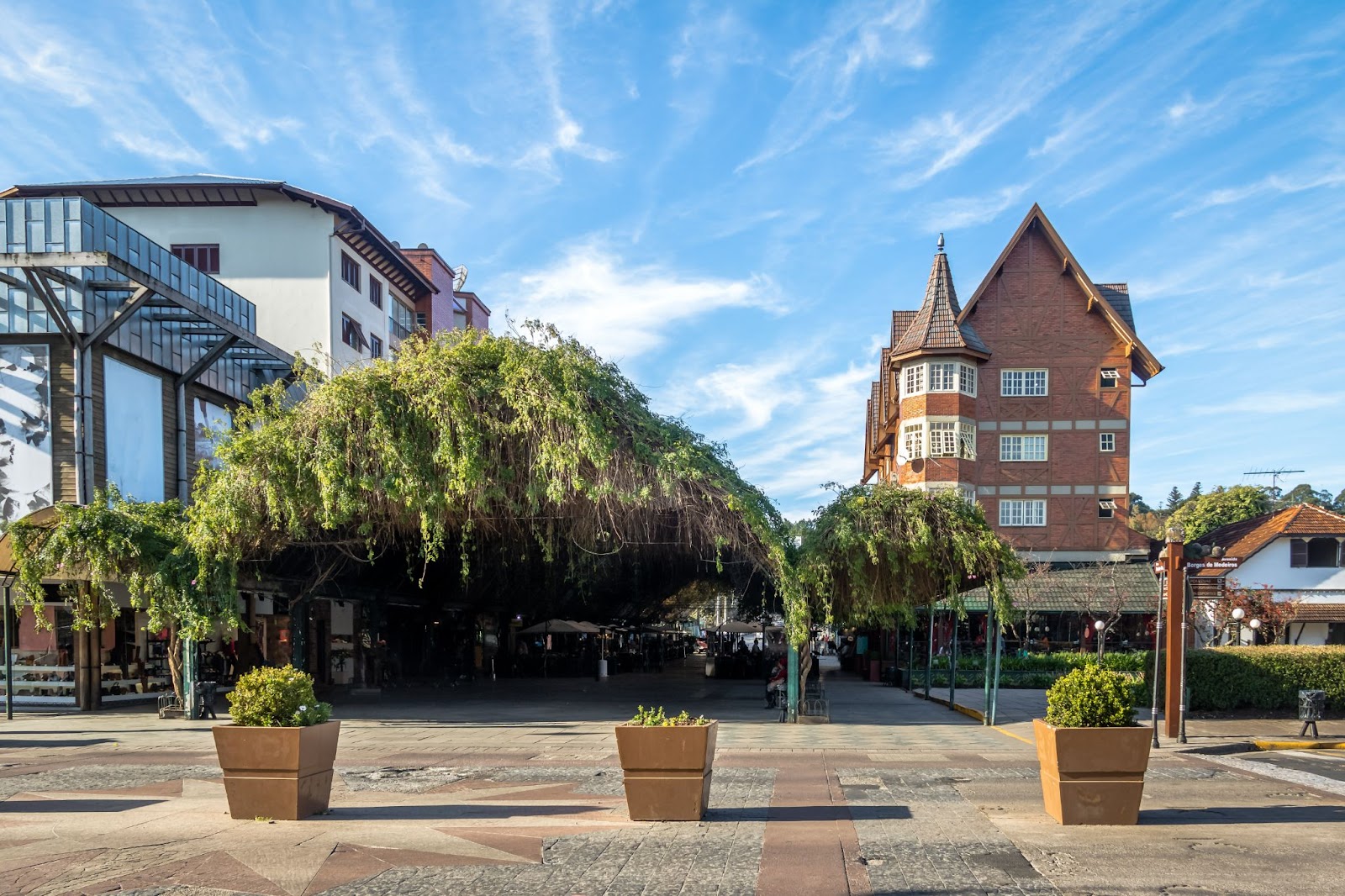 Início da Rua Coberta em Gramado. Estrutura coberta de plantas pendentes, ao lado de construções coloniais.