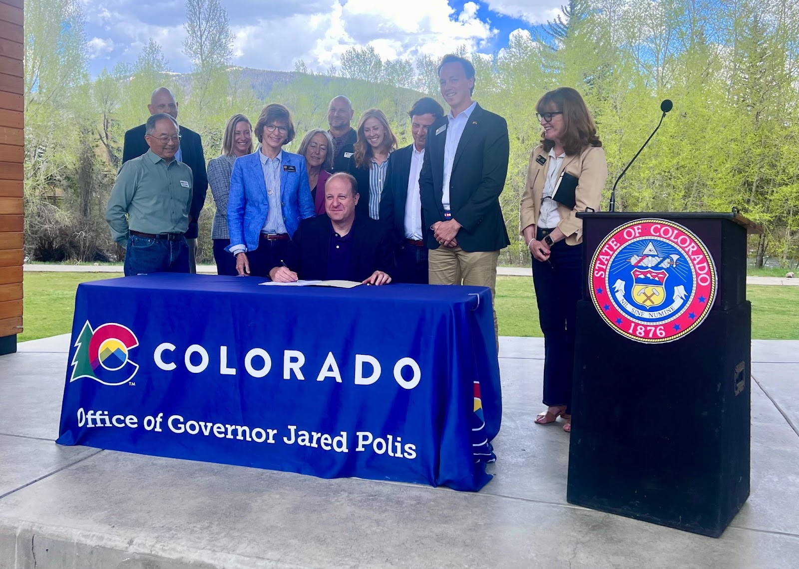 Jared Polis signs the Projects Bill at an outdoor table 