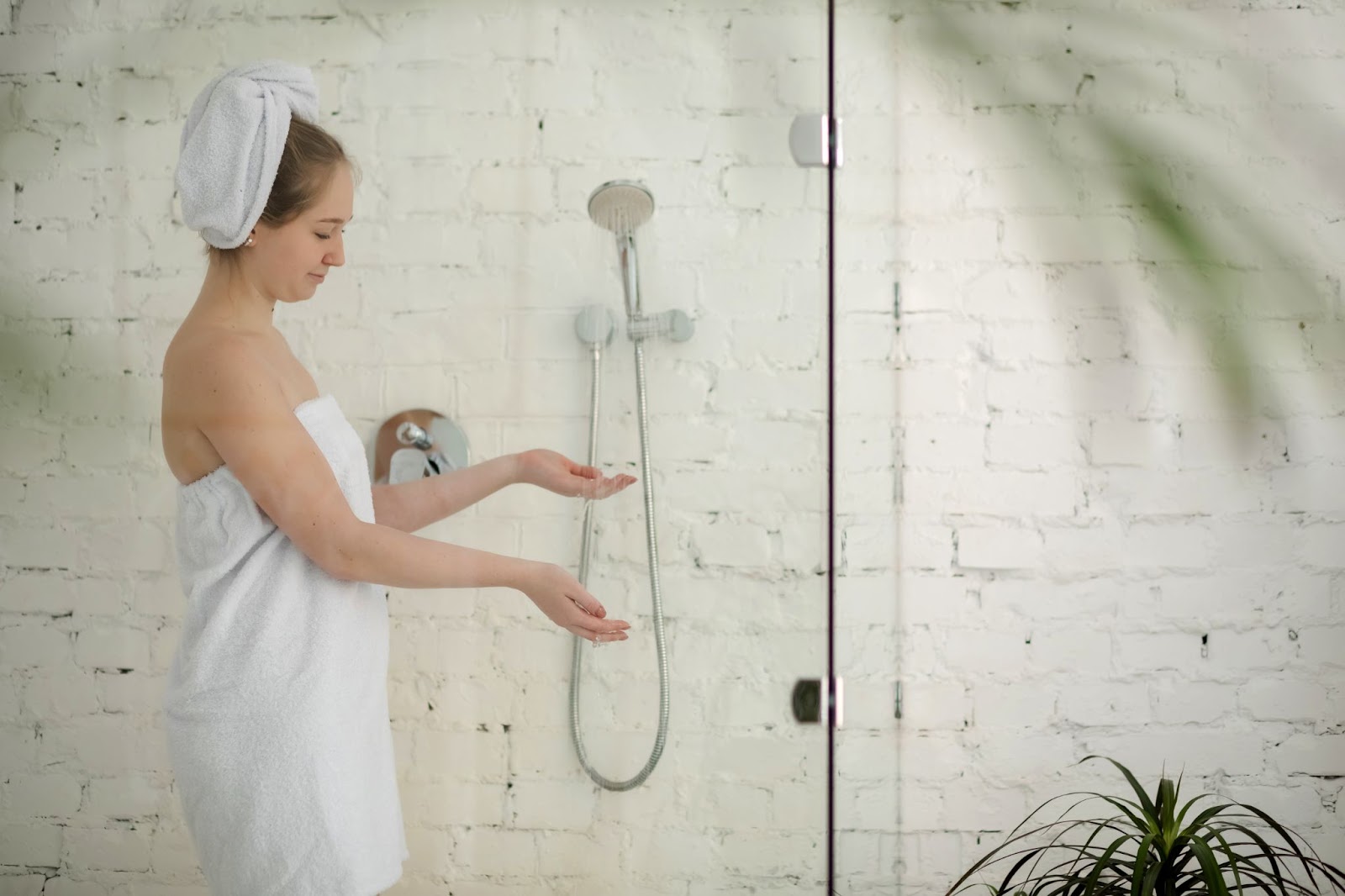 A young woman tests the water flow of a handheld shower set, highlighted against a crisp white background.