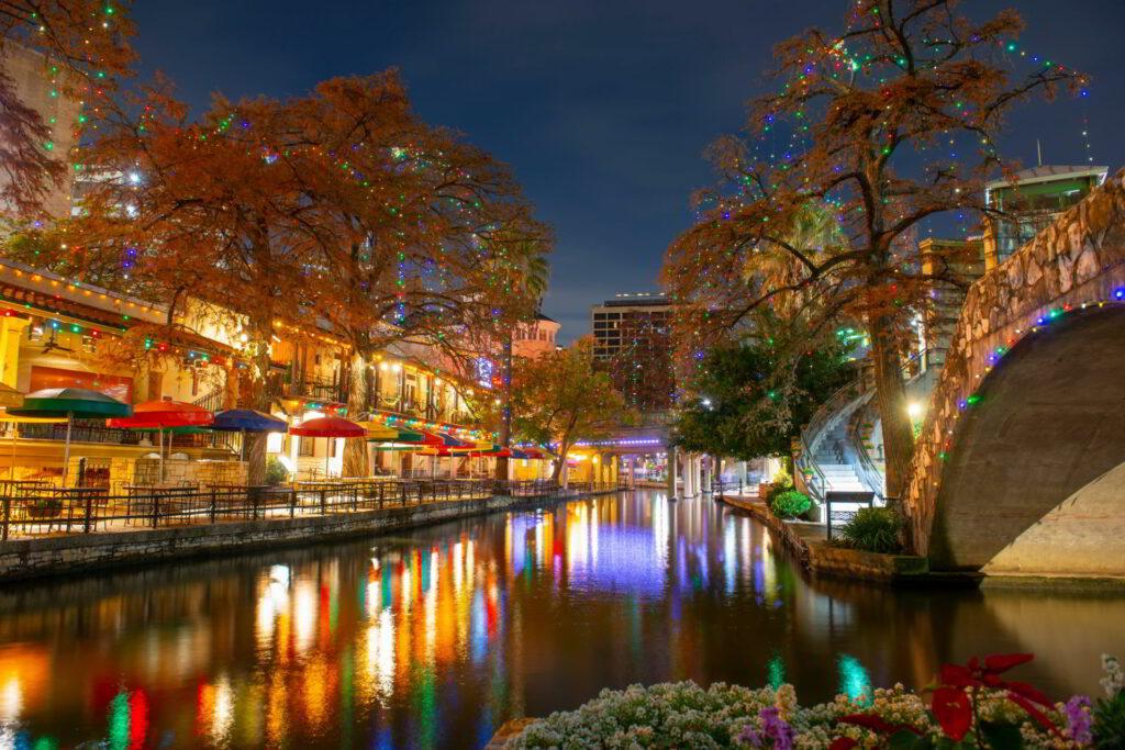 A river with buildings and trees and lights with San Antonio River Walk in the background

Description automatically generated with medium confidence