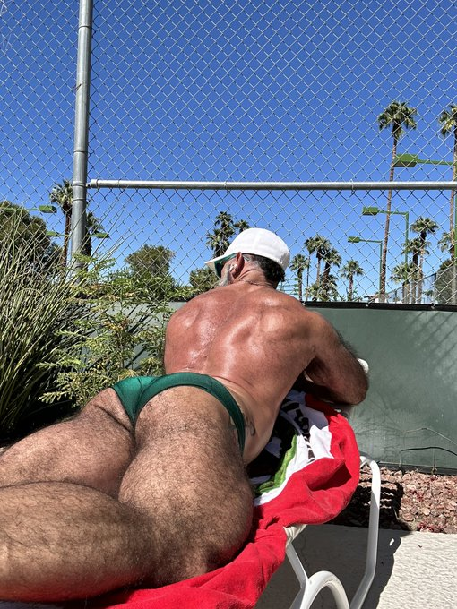 Lawson James lying down on his stomach outside in a green speedo on a beach chair in palm springs