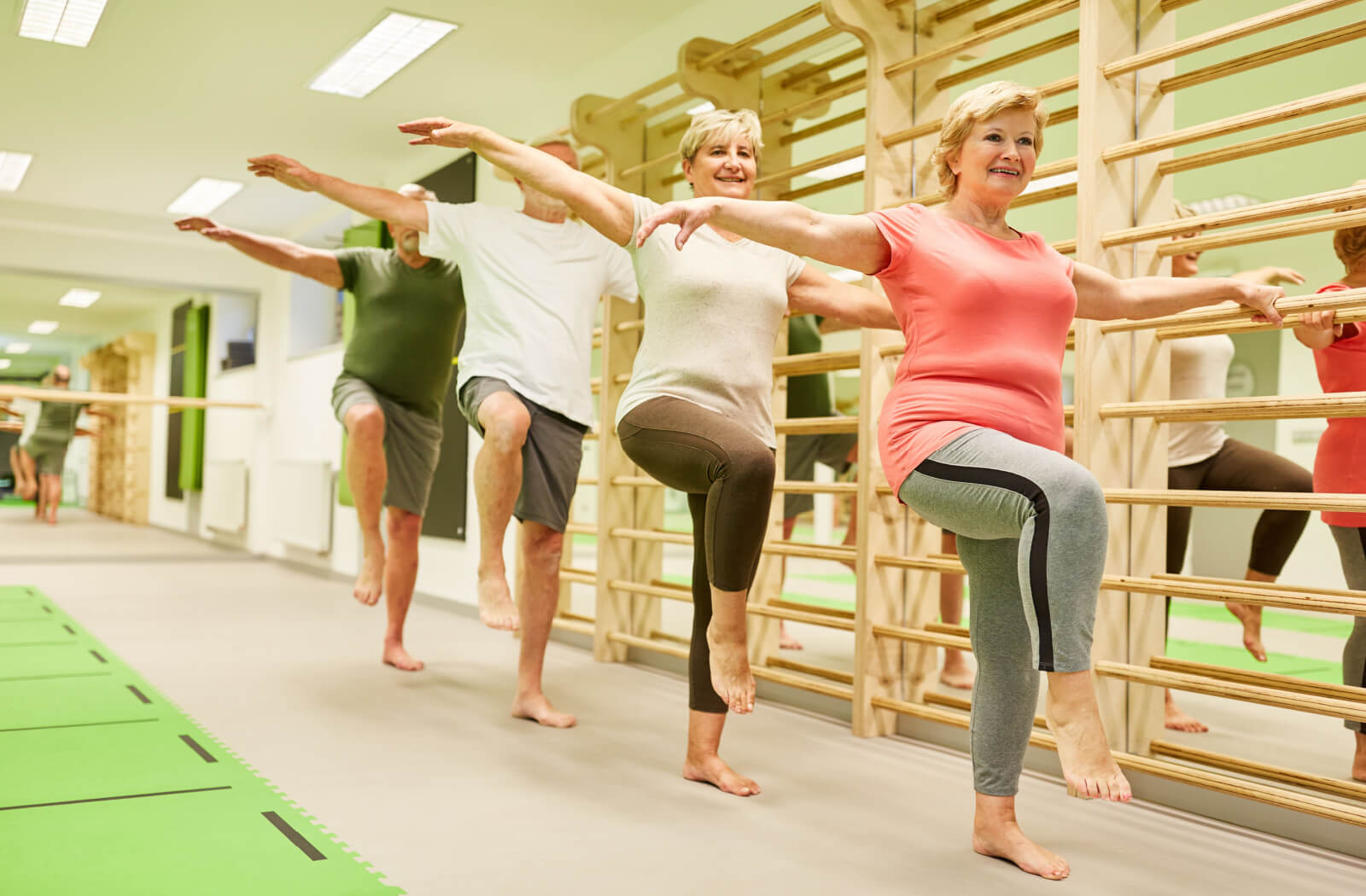 A group of seniors in a group fitness room raises their right arm and right leg as a part of their balancing exercises