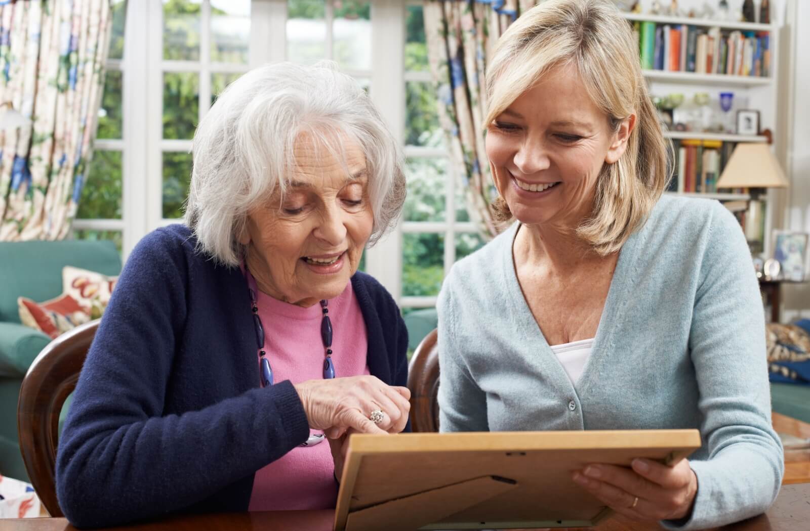 An older adult woman and her middle-aged daughter looking at a photo fondly.