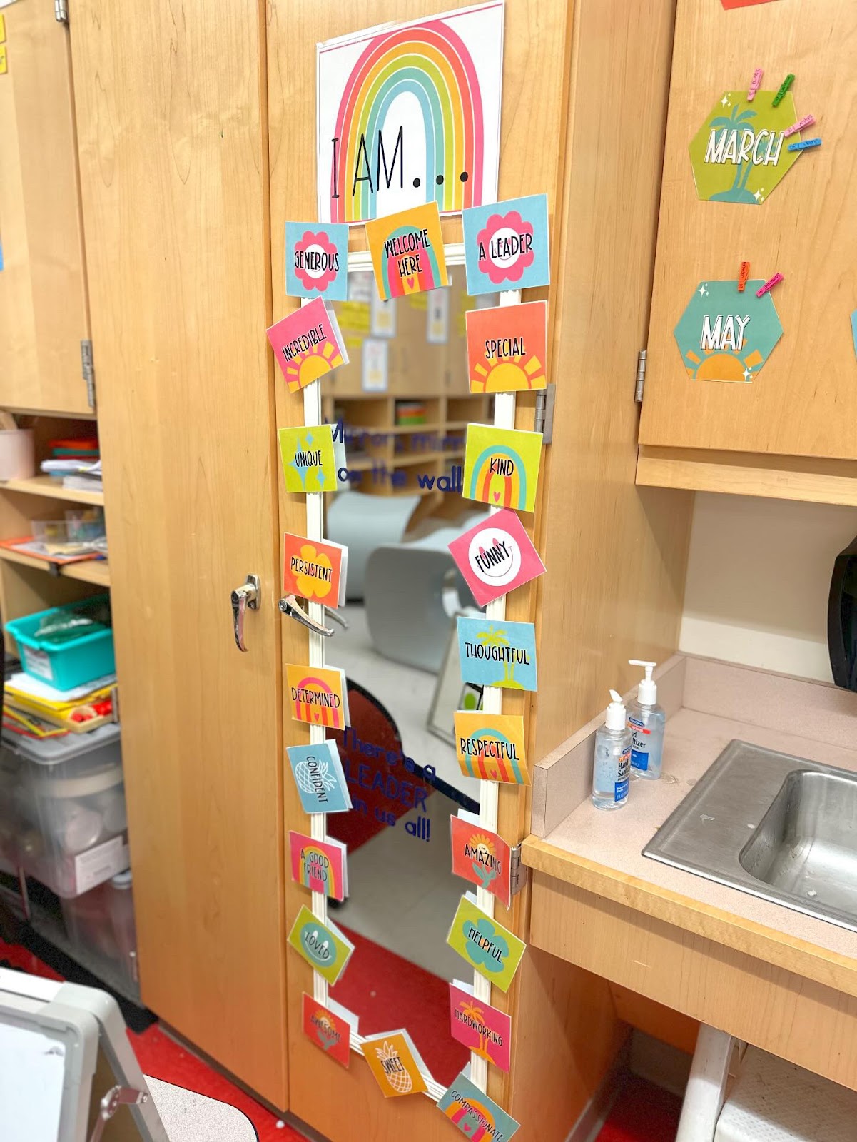 This image shows a closeup of an affirmation station. There is a long, skinny mirror attached to a long cabinet door with small cards taped all the way around the border of the mirror. The cards have different affirmations written on them. 