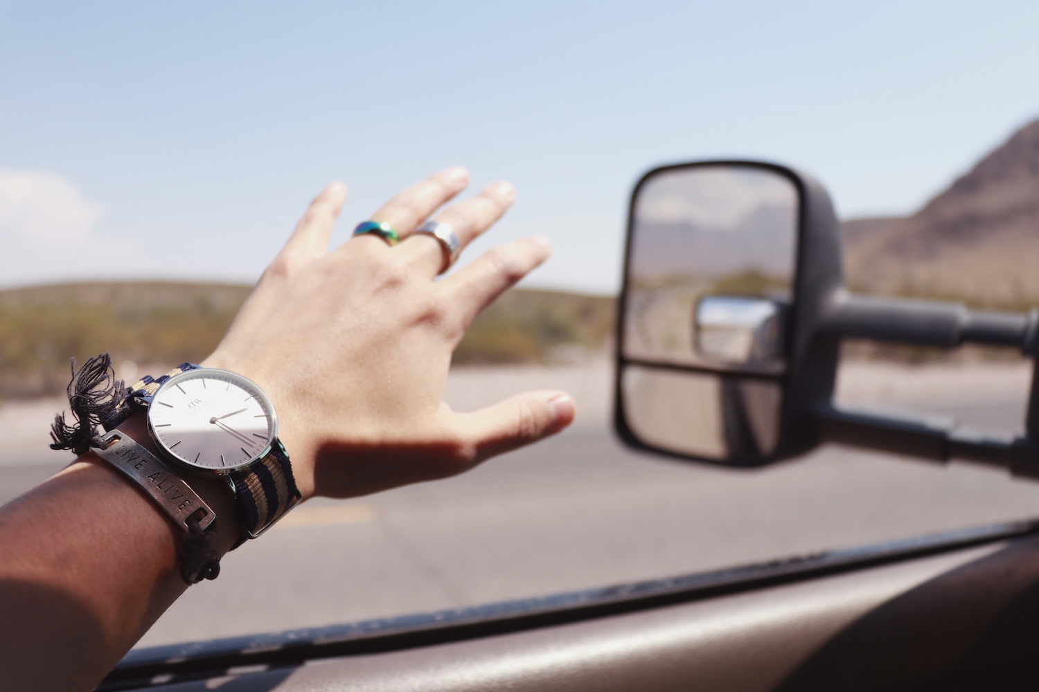 Light-skinned hand with watch and bracelets sticking out of a truck window driving on a sunny day