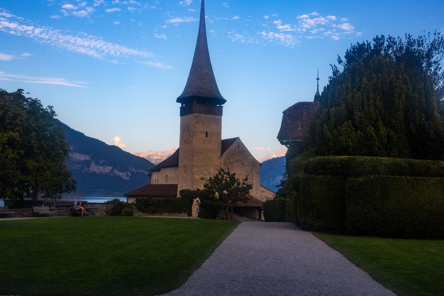 A stone building with a steeple and a path leading to a body of water

Description automatically generated