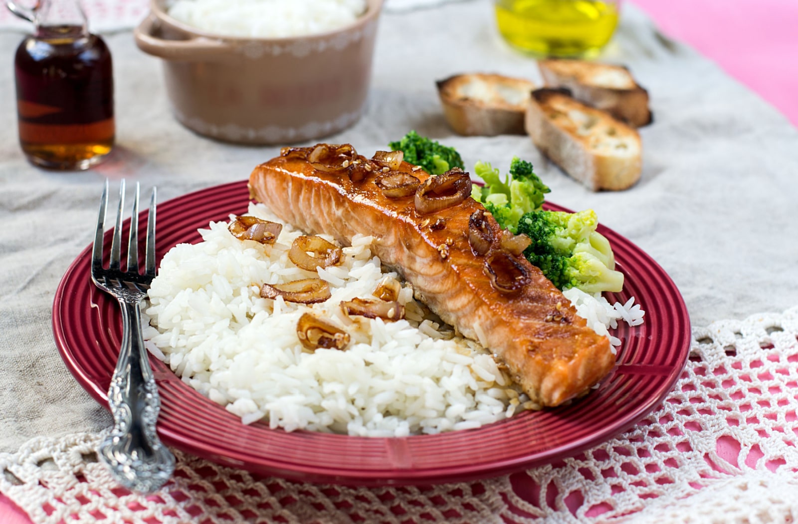 A plate of maple glazed salmon, sitting on a bed of white rice, next to some cooked broccoli. The salmon is also covered with caramelized onions.