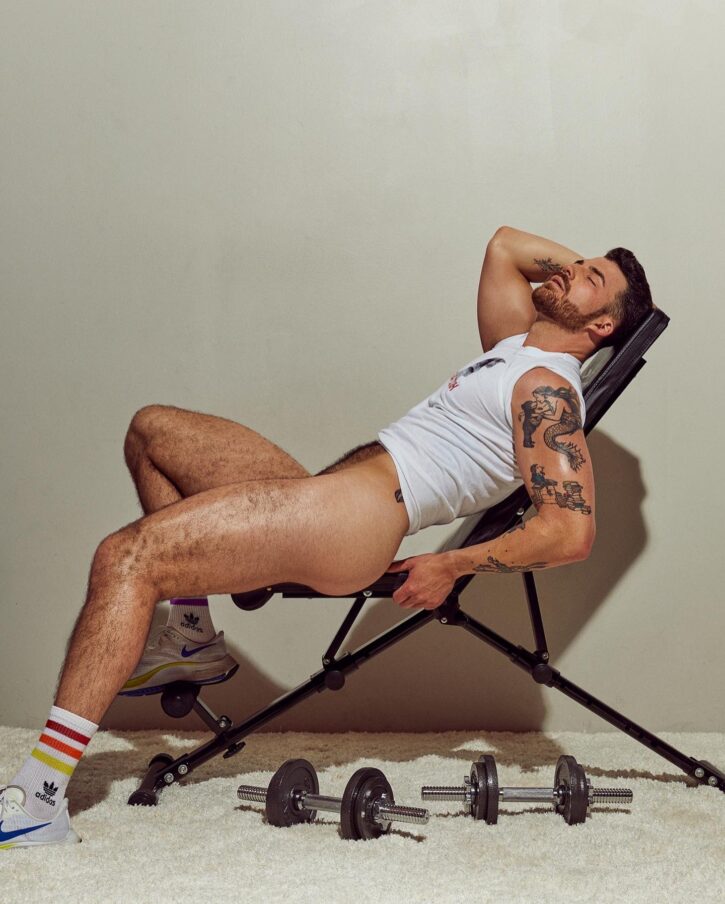 Dillon Cassidy posing in a foding chair wearing adidas athletic socks on soft white rug with dumbbell weights laying beside him