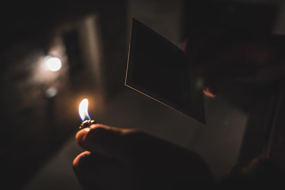 A person is about to burn a picture in his hand with the flame in another hand