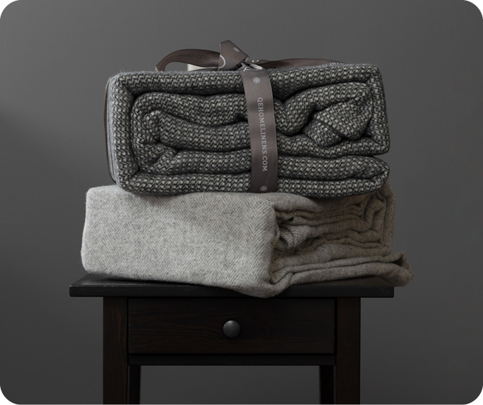 Our dark grey Lismore Wool Blend Blanket shown folded in its packaging resting on top of our light grey Shetland Wool Blend Blanket.