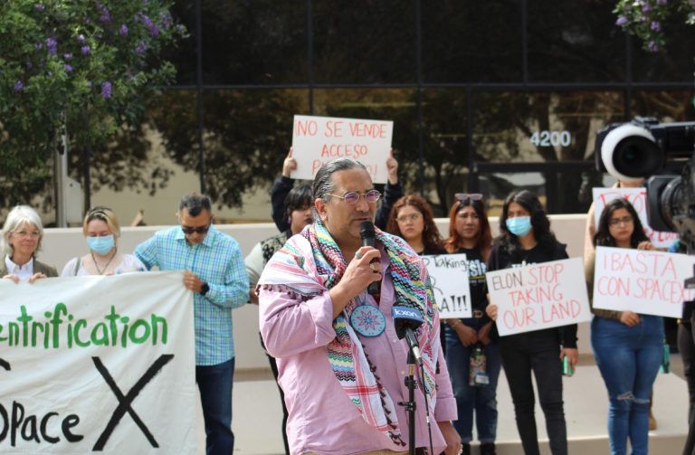 A person standing behind a microphone addressing a crowd of protesters.