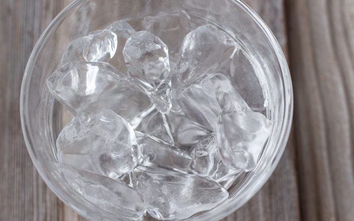 horizontal image of a clear glass bowl with ice cubes on a wooden background