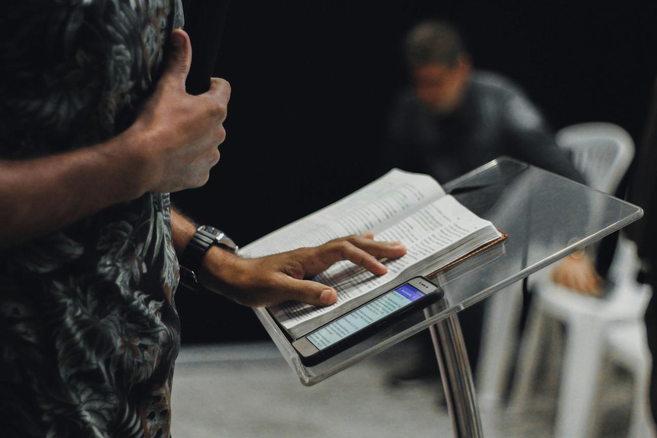 A christian motivational speaker with his bible and phone on a podium on stage delivering his speech.