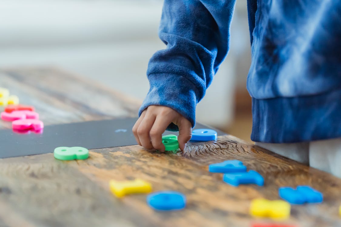 Free Crop anonymous ethnic boy taking plastic number from wooden table while learning math Stock Photo