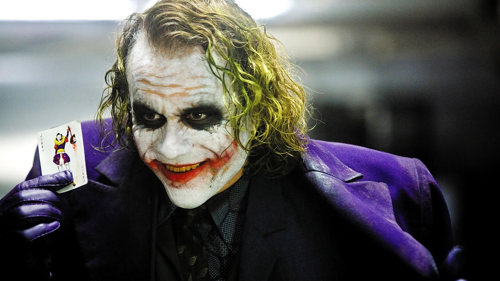 El Joker de Heath Ledger en The dark night, sonriendo con su traje morado y una carta del joker en la mano